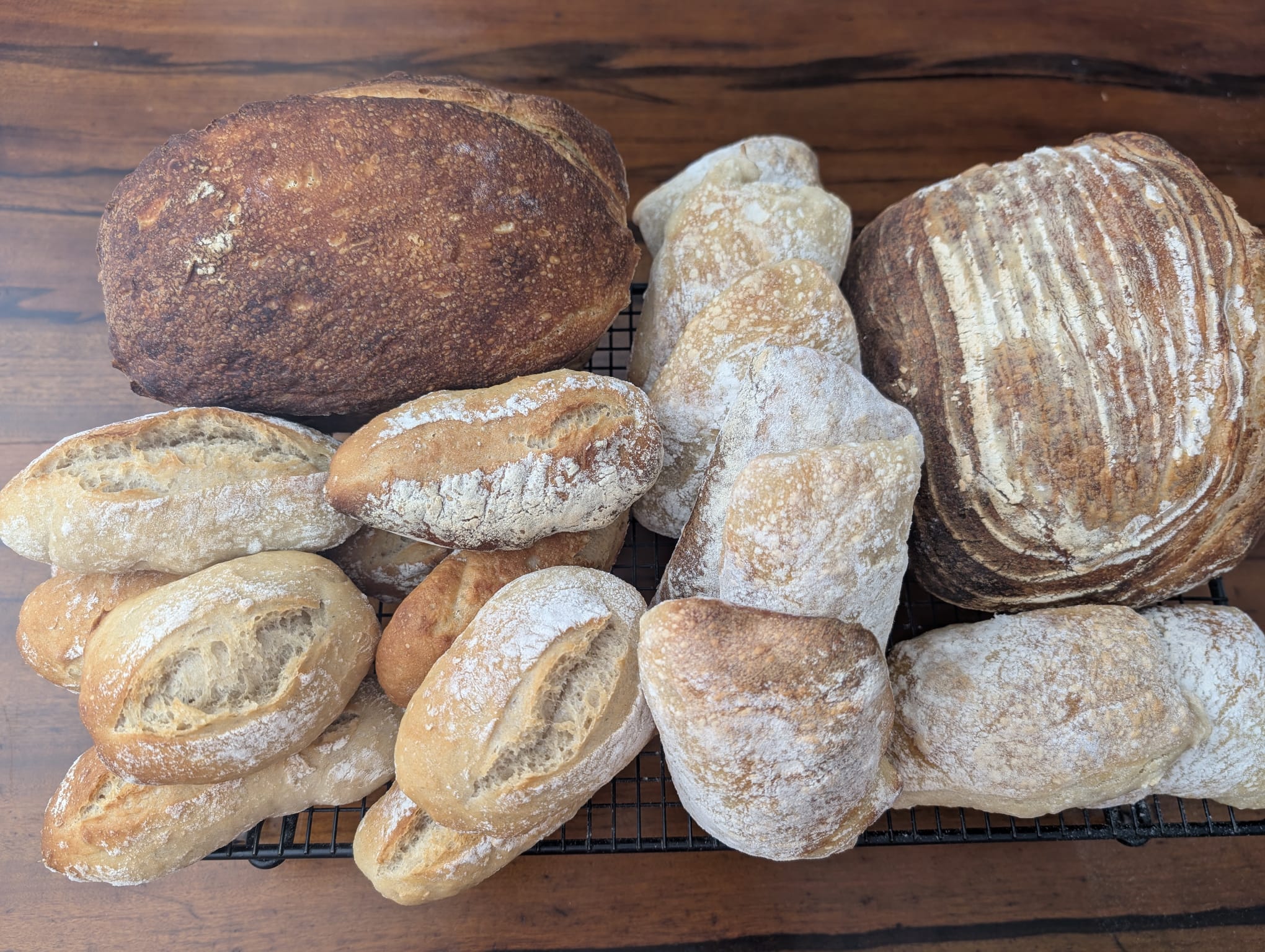 A selection of round loaves and flour-dusted bread rolls on a cooling rack.
