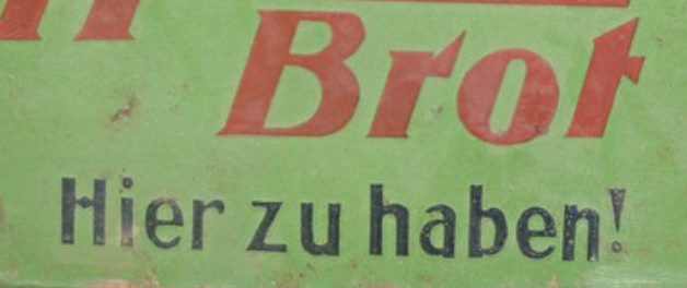 A faded green and red vintage sign reading Brot. Hier zu haben!
